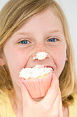 Junges Mädchen beißt in Cupcake mit Zuckerguss auf der Nase
