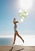 Profile of a woman jumping mid air holding a bundle of green balloons