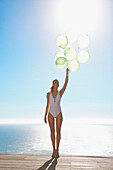 Woman standing on a sun deck holding a bundle of green balloons