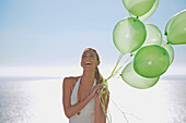 Nahaufnahme einer Frau, die ein Bündel grüner Luftballons hält und lächelt