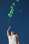 Frau lässt grüne Luftballons bei wolkenlosem Himmel aufsteigen - Blick aus geringer Höhe