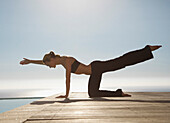 Junge Frau übt Yoga an einem Swimmingpool mit dem Meer im Hintergrund