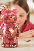 Girl putting coins into a money box in the shape of a teddy bear
