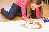 Mädchen kniet auf dem Boden und malt mit Aquarellfarben