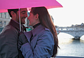 Close up of a couple hugging under a pink umbrella by the Seine river, Paris, France