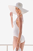 Porträt einer Frau im weißen Badeanzug, die die Krempe ihres Hutes hält
