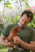Mann hält braunes Huhn