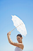 Braut hält Sonnenschirm gegen blauen Himmel