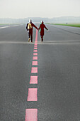 Paar läuft händchenhaltend die Start- und Landebahn entlang, Rückansicht