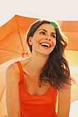 Lächelnde Frau unter orangefarbenem Sonnenschirm