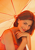 Lächelnde Frau unter orangefarbenem Sonnenschirm