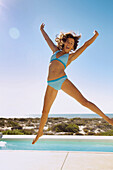 Lächelnde junge Frau, die im Schwimmbad in der Luft springt