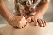 Nahaufnahme Massagetherapeutin massiert Rücken eines Mannes mit Faust