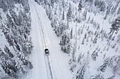 Luftaufnahme eines Autos, das den mit Schnee bedeckten borealen Wald durchquert, Akaslompolo, Finnisch Lappland, Finnland, Skandinavien, Europa