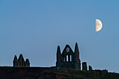 Half moon rising over Whitby Abbey in mid-October 2023, North Yorkshire coast, Whitby, Yorkshire, England, United Kingdom, Europe