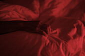 Hand einer nicht identifizierten Person im Bett unter rotem Licht