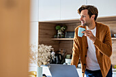 Nachdenklicher junger Mann trinkt eine Tasse Kaffee, während er in der Küche steht