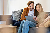 Erwachsenes Paar nutzt ein digitales Tablet, während es sich tagsüber auf dem Sofa entspannt