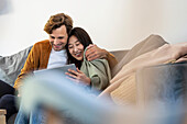 Erwachsenes Paar kuschelt bei der Nutzung eines digitalen Tablets im Wohnzimmer