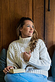 Beautiful woman sitting on bed with a book while looking away