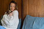 Porträt einer frierenden Frau, die sich umarmt, während sie auf dem Bett sitzt