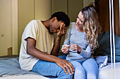 Enttäuschter Mann mit Hand im Gesicht, der mit einem Schwangerschaftstest neben seiner Freundin sitzt