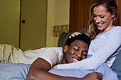 Fröhlicher Mann mit Kopf auf dem Bauch seiner Freundin, während er sich im Bett umarmt