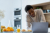 Erwachsener Mann benutzt Laptop, während er sich an den Küchentresen lehnt