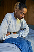 Young adult woman having a stomachache while sitting on bed