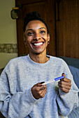 Fröhliche Frau schaut nach oben, während sie einen Schwangerschaftstest hält
