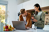 Erwachsenes Paar beim Online-Shopping mit Laptop und Smartphone am Küchentisch