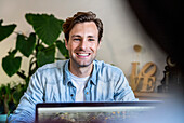 Cheerful male graphic designer sitting at desk using laptop