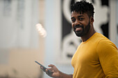 Afroamerikanischer Mann schaut in die Kamera, während er ein Smartphone hält