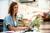 Erwachsene weibliche Grafikdesignerin, die am Schreibtisch sitzend einen Laptop benutzt