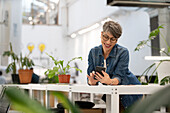 Unternehmerin scrollt auf dem Smartphone, während sie sich auf einen Tisch stützt