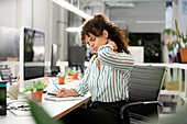 Gestresste Frau mit einer Nackenkontraktur im Büro sitzend