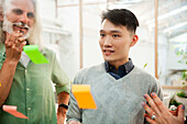 Coworker brainstorming while writing on sticky notes on glass wall