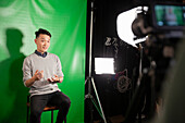 Young adult man giving an interview while sitting against green screen