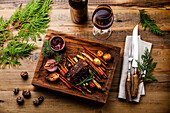 Grilled venison steak with baked vegetables and berry sauce and red wine on a wooden base