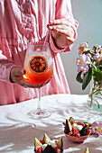 Aperol Spritz-Cocktail, auf zartrosa Leinentischdecke, Schatten, Sonnenlicht, Sommerdrink im Glas