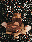 Travel Cake or Tube Cake or Voyage Cake, filled with ganache in the centre and topped with chocolate icing and pistachios (can also be made with peanuts). Chocolate cake with chocolate cream cheese filling in the centre. Idea and recipe for baking with ganache cream centre. Loaf cake on women's hands