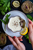 Women's hands serving a bowl of artichoke sauce on a plate