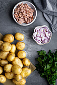 Abgetropfter Thunfisch in einer Schüssel, Babykartoffeln, geschnittene Zwiebeln und Petersilie, von oben fotografiert