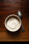 Bowl of yoghurt on antinque wooden table with silver spoon.