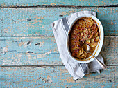 Top view image of potato gratin in white baking dish on wooden background with copy space