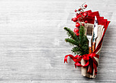 Tischgabel und Messerset mit Serviette, Weihnachtstannenzweig, roten Beeren und Band auf grauem Holzhintergrund Copy Space
