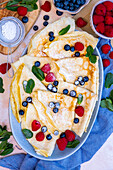 Crepes topped with raspberries, blueberries and fresh mint served on a large oval plate.