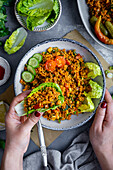 Woman hands holding a lettuce leaf stuffed with bulgur salad over a bowl of bulgur salad, more lettuce leaves on the side.