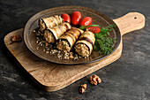 Grilled eggplant rolls stuffed with walnuts with tomatoes and fresh green dill. The plate is on the cutting board.