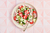 Spring salad with strawberries, cucumber, radish and parsley on pink tiles